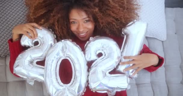 Black woman lying on a bed holding 2021 balloons — Stock Video