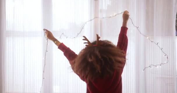 Zwarte vrouw draagt rendier gewei hoofdband dansen met kerstverlichting — Stockvideo