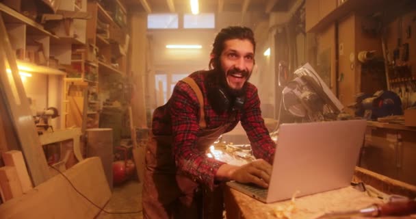 Homme en atelier de menuiserie souriant à l'aide d'un ordinateur portable — Video