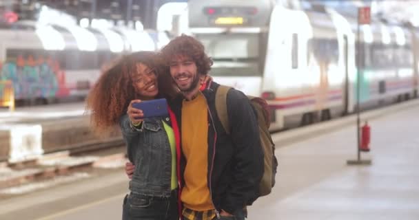Wieloetniczna para robi selfie ze smartfonem na dworcu kolejowym — Wideo stockowe