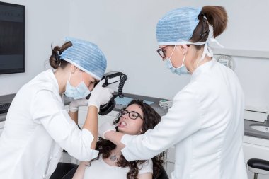 Kadın dişçi ve asistan dişçi muayenehanesinde çalışırken genç bayanın fotoğrafını çekiyorlar.