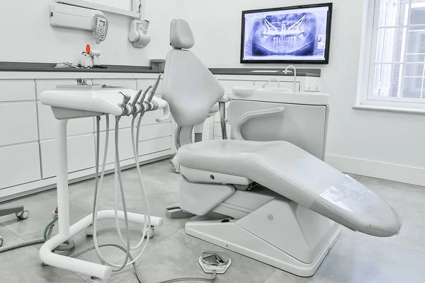 White dental chair and set of professional tools located near cabinets and computer monitor with teeth X ray inside light dentist office
