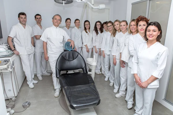 白い制服を着た男性と女性の歯科医のグループ笑顔とカメラを見ながら 現代の歯科クリニックのオフィスの椅子の近くに立って — ストック写真