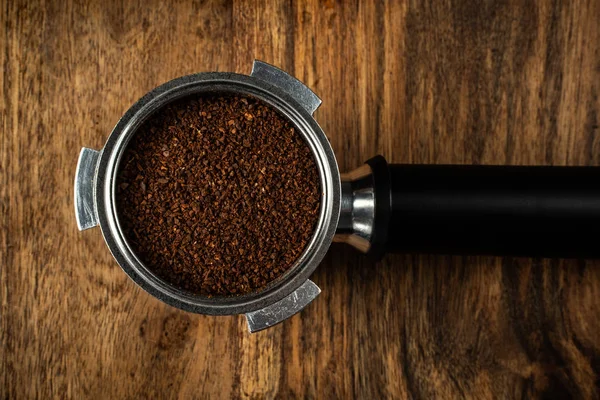Above view of a coffee filter holder filled with ground coffee on a wooden table.