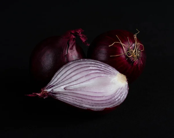 Half a red onion and two red onions isolated on a black background