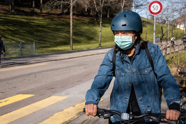 A woman is wearing a face mask while riding a bicycle.