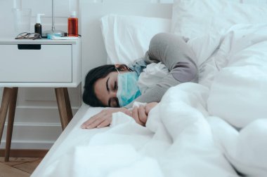 Genç, hasta bir kadın yüzünde maskeyle yatakta uyuyor..