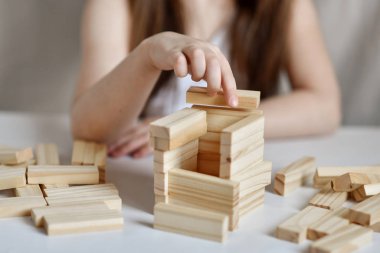 Küçük kız arka planda beyaz giysiler içinde jenga oynuyor.