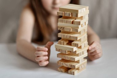 Küçük kız arka planda beyaz giysiler içinde jenga oynuyor.