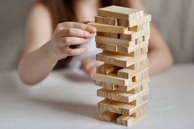 Küçük kız arka planda beyaz giysiler içinde jenga oynuyor.