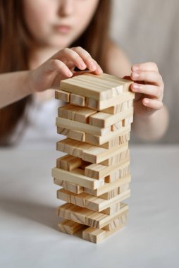 Küçük kız arka planda beyaz giysiler içinde jenga oynuyor.