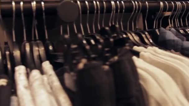 Filas de ropa en perchas cuelgan en una tienda. Vista dentro del centro comercial . — Vídeo de stock