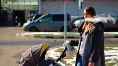 Sorumsuz bir anne sigara içer ve etrafa bakar. Bebek arabasındaki bebek