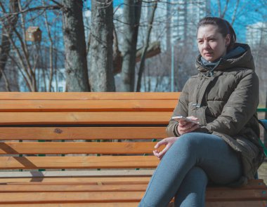 Güzel, genç bir şehir kadını elinde telefonla bankta oturuyor.