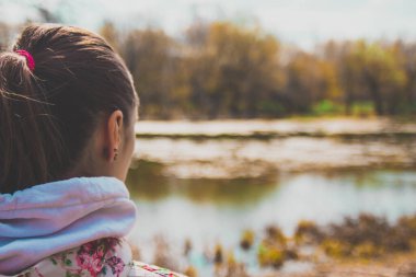 Genç bir kadın gölün kenarında duruyor ve uzaklığa bakıyor. Arka plan.