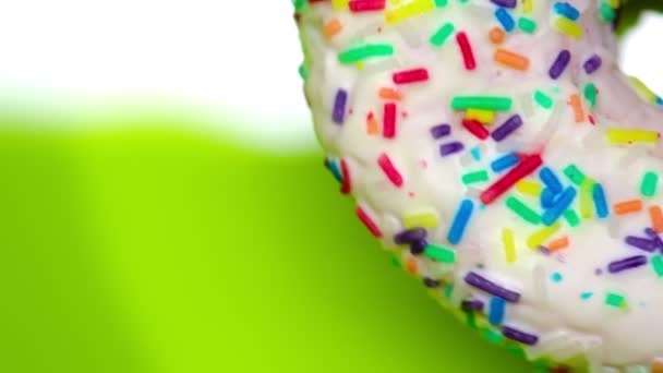 White donut with colored sprinkles rotates on a green background copy space — Stock Video