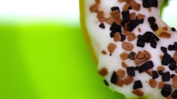 Close-up white donut with brown topping sprinkles on a green background copy space — Stock Video