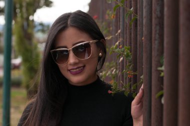 Siyah arka planda siyah ceketi olan ve gözlük takan Ekvadorlu kadın.