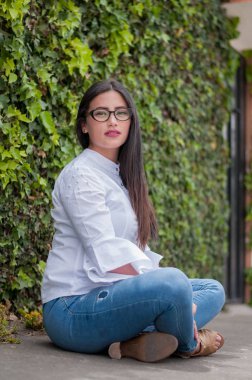 Doğada poz veren profesyonel bir kız. Beyaz tişörtlü ve kameraya bakan zarif gözlüklü güzel Latin kadın. Kadın portresi kavramı