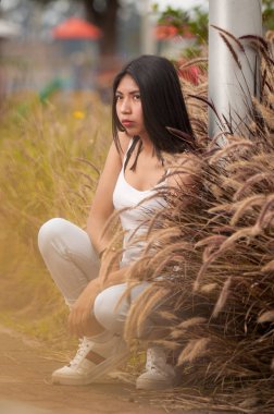 Genç Latin, kısa siyah saçlı, kahverengi çiçeklerin yanında oturuyor.