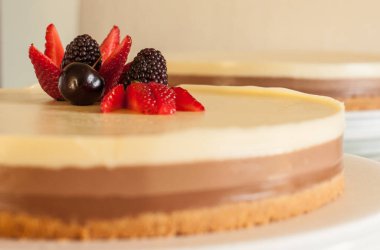 Bisküvi parçacıklı üç farklı çikolatalı kek ve beyaz bir tabakta çilekli kiraz ve çilekle süslenmiş.