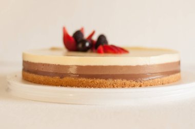 Bisküvi parçacıklı üç farklı çikolatalı kek ve beyaz bir tabakta çilekli kiraz ve çilekle süslenmiş.
