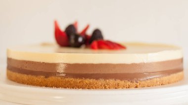 Bisküvi parçacıklı üç farklı çikolatalı kek ve beyaz bir tabakta çilekli kiraz ve çilekle süslenmiş.