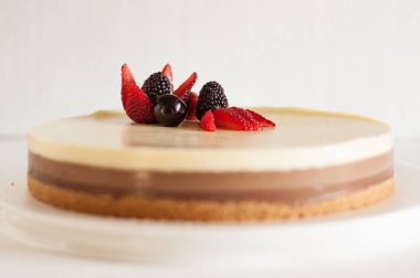 Bisküvi parçacıklı üç farklı çikolatalı kek ve beyaz bir tabakta çilekli kiraz ve çilekle süslenmiş.