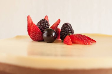 Bisküvi parçacıklı üç farklı çikolatalı kek ve beyaz bir tabakta çilekli kiraz ve çilekle süslenmiş.