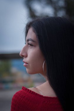 Bir parkın ortasında, arka planda dikkatsiz bir şekilde oturan genç Latin kız arkasını dönüyor.