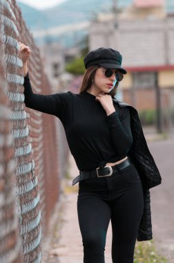 Siyah şapkalı, siyah tişörtlü ve raflarda dinlenen güneş gözlüklü güzel bir kadın portresi.