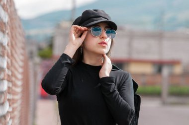 Siyah şapkalı, siyah tişörtlü ve raflarda dinlenen güneş gözlüklü güzel bir kadın portresi.