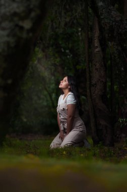 Joven mujer arrodillada en medio del bosque mirando hacia arriba