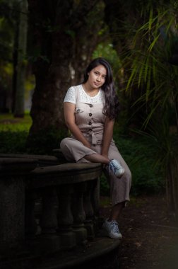 Siyah arka planda parkın ortasında oturan genç bir kadının portresi.