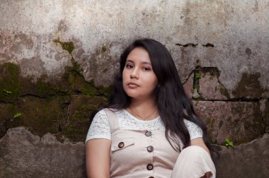 Genç bir kadının portresi oturuyor ve eski bir duvara yaslanıyor.