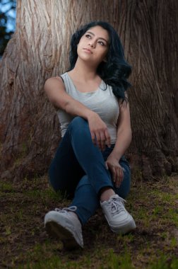 Genç siyah saçlı Latin bir ağaca yaslanıp oturuyor.