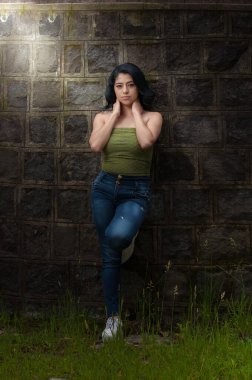 Genç siyah saçlı Latin, taş duvar manzarasına yaslanıyor.