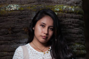 Genç siyah saçlı latin, siyah arka planı olan bir ağaca yaslanıyor.