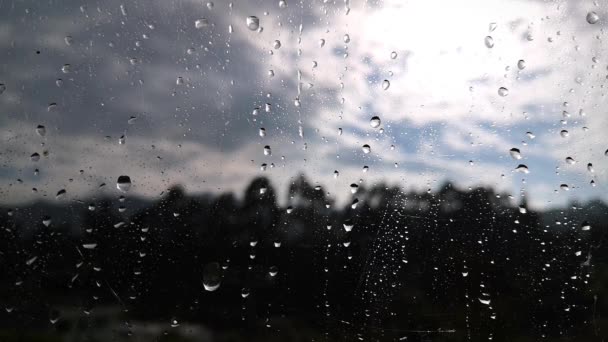 Gocce di pioggia che cadono su una finestra con uno sfondo sfocato di una montagna — Video Stock