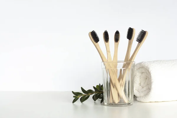 Bambu diş fırçaları açık gri masada, üzerinde havlu ve yeşil dal bulunan camlarda durur. Sıfır atık ev, çevre dostu banyo aksesuarları ve sürdürülebilir yaşam tarzı konsepti. Boşluğu kopyala.