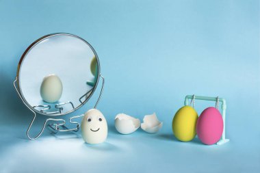 Paskalya yaratıcı konsepti. Gözleri haşlanmış yumurta ve gülümseme renkli yumurta kabuğunun askıda asılı olduğu soyunma odasının aynasının yanında duruyor. Boşluğu kopyala.