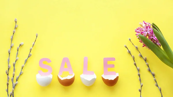 Easter composition made of pink letters SALE, broken egg shell, hyacinth flower and pussy-willow twigs on yellow background. Spring, Easter sale concept. Flat lay, top view, copy space.
