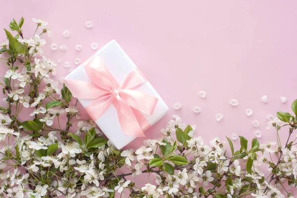 Beyaz hediye ya da pembe kurdeleli hediye kutusu ve pastel pembe arka planda çiçek açan kiraz dalları. Uzayı kopyala Anneler Günün kutlu olsun, Kadınlar Günü ya da Doğum Günü Bahar tebrik kartı.
