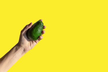 Sarı arka planda kadın avakado tutuyor. Parlak güneş ışığı, gölgeler ve kontrastlar. Sağlıklı ve vejetaryen yiyecekler minimum konsept. Boşluğu kopyala.