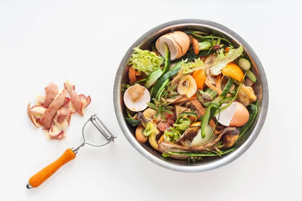 Organic food waste in iron bowl, potato peeling and knife on white table. Food leftovers ready to compost. Environmentally responsible behavior, ecological, recycling waste concept. Copy space.