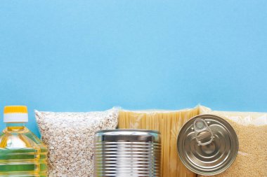 Makarna, yulaf ezmesi, kuskus, yağ ve mavi arka planda konserve yiyecekler. Yemek teslimatı, bağış konsepti. Karantina için yiyecek stoku. Boşluğu kopyala.