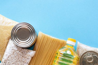 Paketlerdeki çeşitli bakkal ürünlerinden yapılmış sınır çerçevesi. Makarna, mısır gevreği, yağ ve mavi arka planda konserve yiyecek. Yiyecek teslimatı, bağış veya hisse senedi konsepti. Üst görünüm, alanı kopyala.