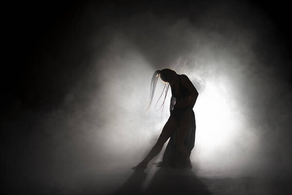 Silhouette dancer woman performing dance figures in fog.