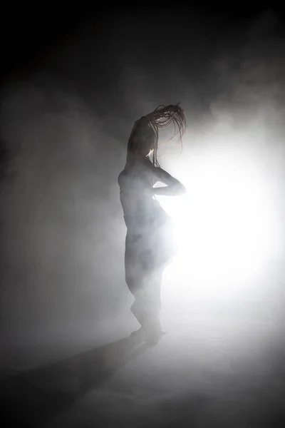 Siluet dansçısı kadın sis içinde dans figürleri sergiliyor.. — Stok fotoğraf