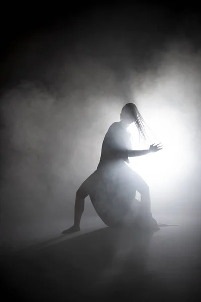 Silhouette dancer woman performing dance figures in fog. — Stock Photo, Image